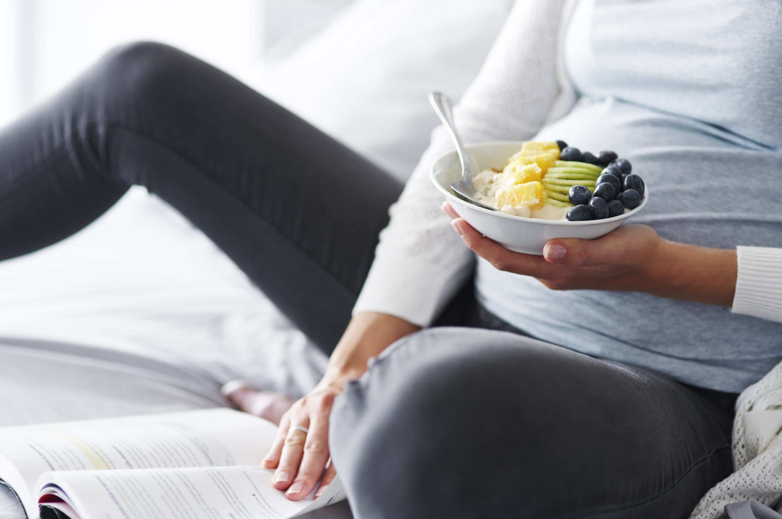 Pregnant woman eating and reading a book at bedroom