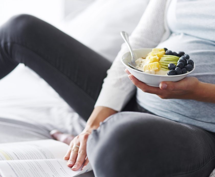 Pregnant woman eating and reading a book at bedroom