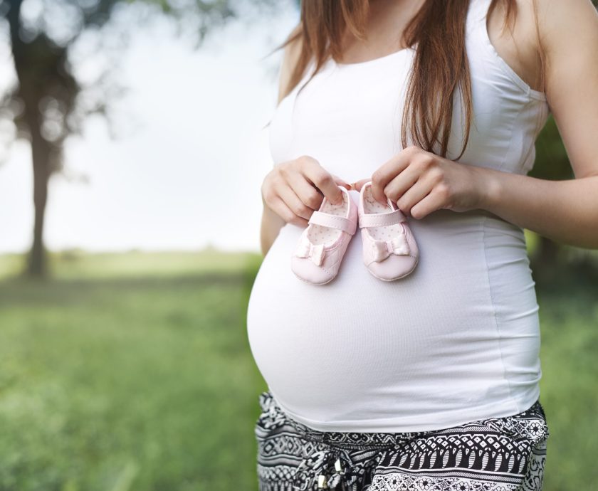 Part of pregnant woman with little shoes for baby