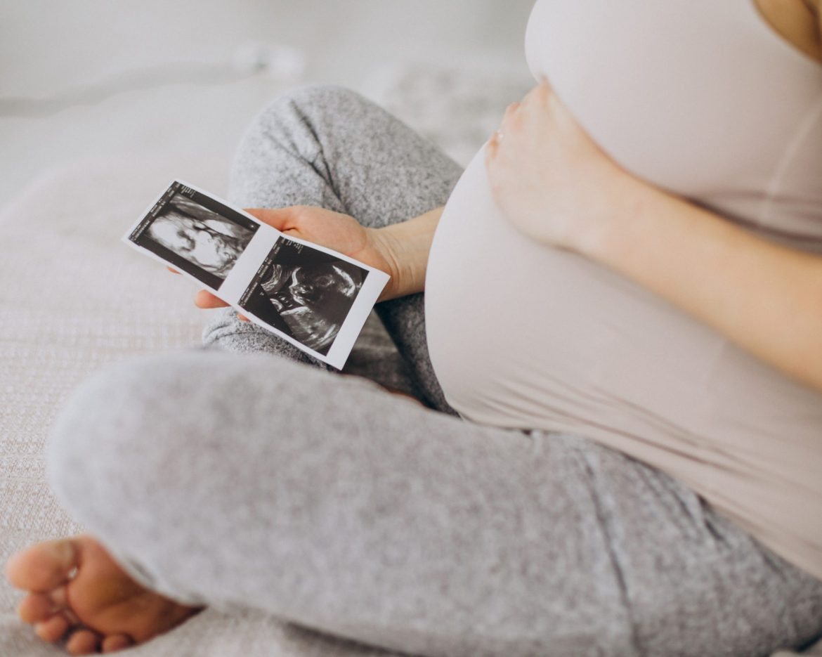 Pregnant woman with ultrasound photo sitting on bed