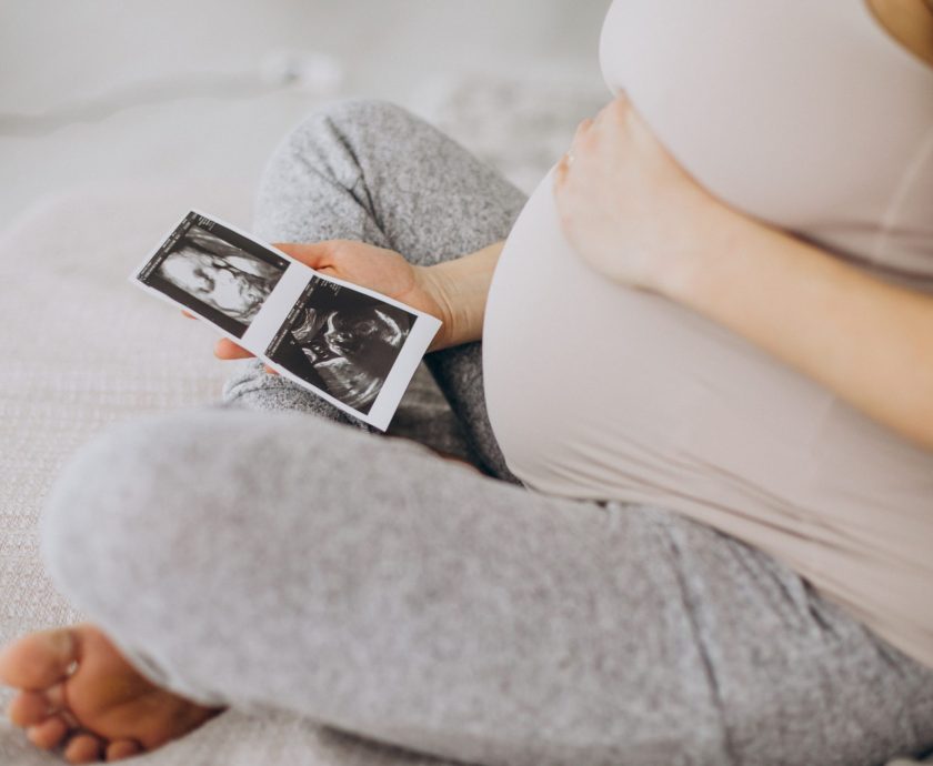 Pregnant woman with ultrasound photo sitting on bed